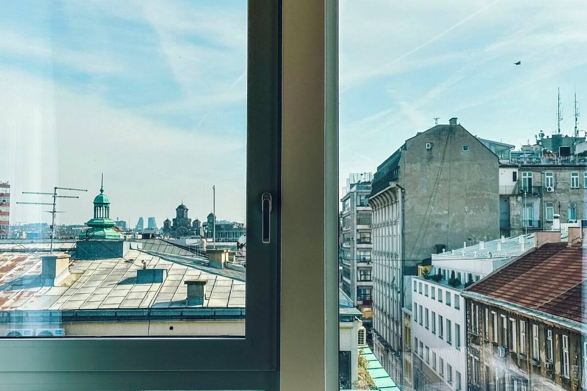 Vista desde una ventana con vista a un paisaje urbano con edificios históricos y cielo despejado.