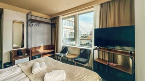 A hotel room with a bed, a TV, a desk, a chair, a small table, and a window with a view of buildings. - Circel of 2 (Belgrade)