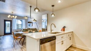 Une cuisine moderne dotée d’un îlot central, d’un lave-vaisselle intégré et d’un évier avec un robinet. On y trouve également un coin repas avec une table et des chaises, ainsi qu’un salon avec un canapé et une table basse.