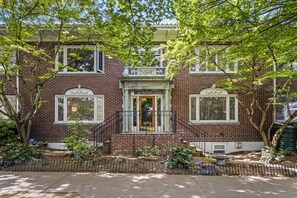A two-story brick house with a front porch, a small garden, and a metal fence.