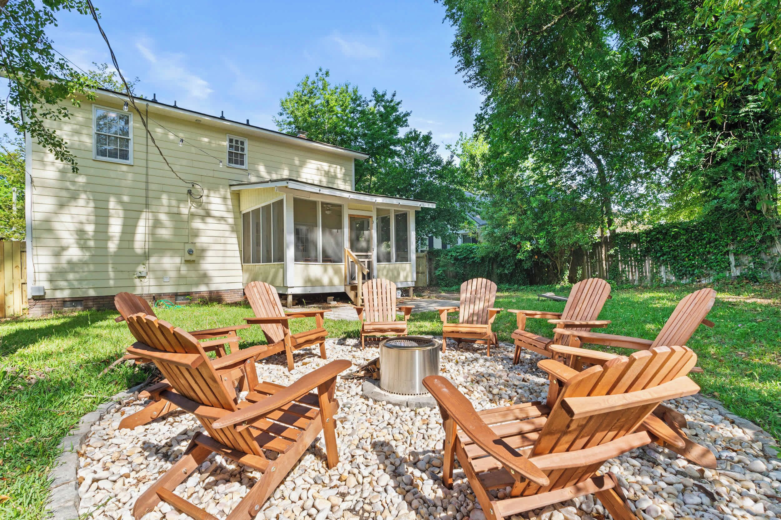 Eine Terrasse mit Holz-Adirondack-Stühlen und einer Feuerstelle, umgeben von einem Kiesbereich und einem Haus mit einer Veranda.