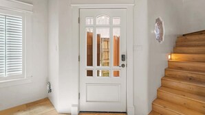 Une porte blanche avec un panneau de verre et un escalier en bois sur la droite.