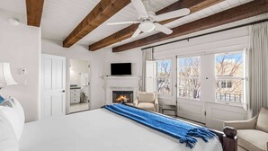 Une chambre spacieuse dotée d’un grand lit, d’une cheminée, d’une télévision et offrant une vue sur l’extérieur grâce à de grandes fenêtres.