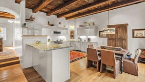 Une cuisine spacieuse avec des meubles blancs, un plafond en bois et un coin repas comprenant une table et des chaises en bois.