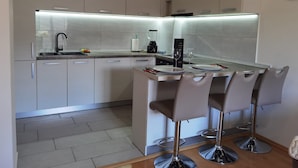 A modern kitchen with a central island, bar stools, and a built-in oven. - Studio Dunja (Niksic)