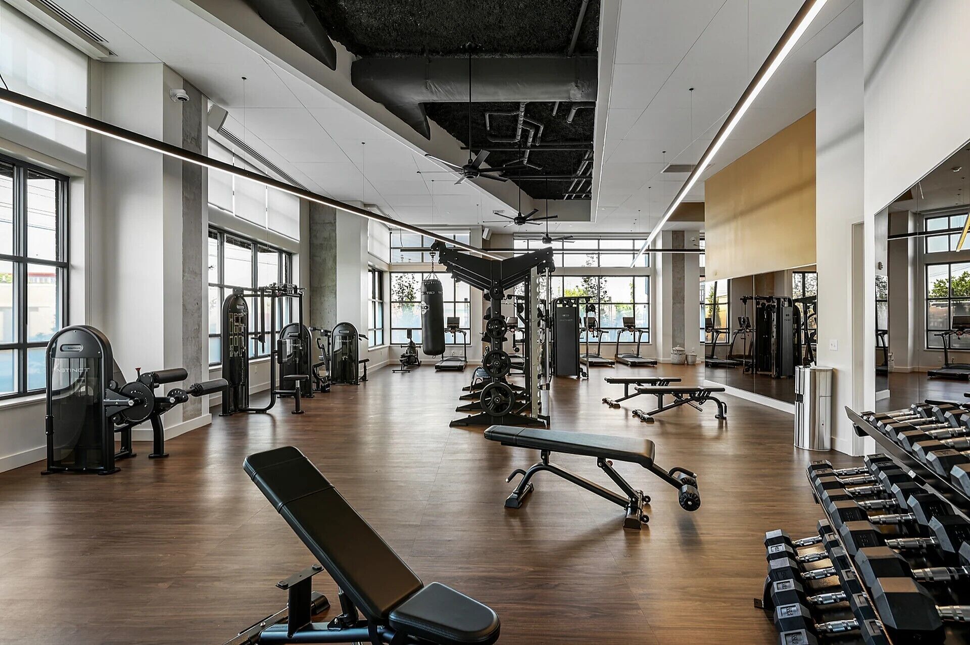 Une salle de sport spacieuse, dotée de divers appareils d’entraînement, de grandes fenêtres et d’un plafond haut.