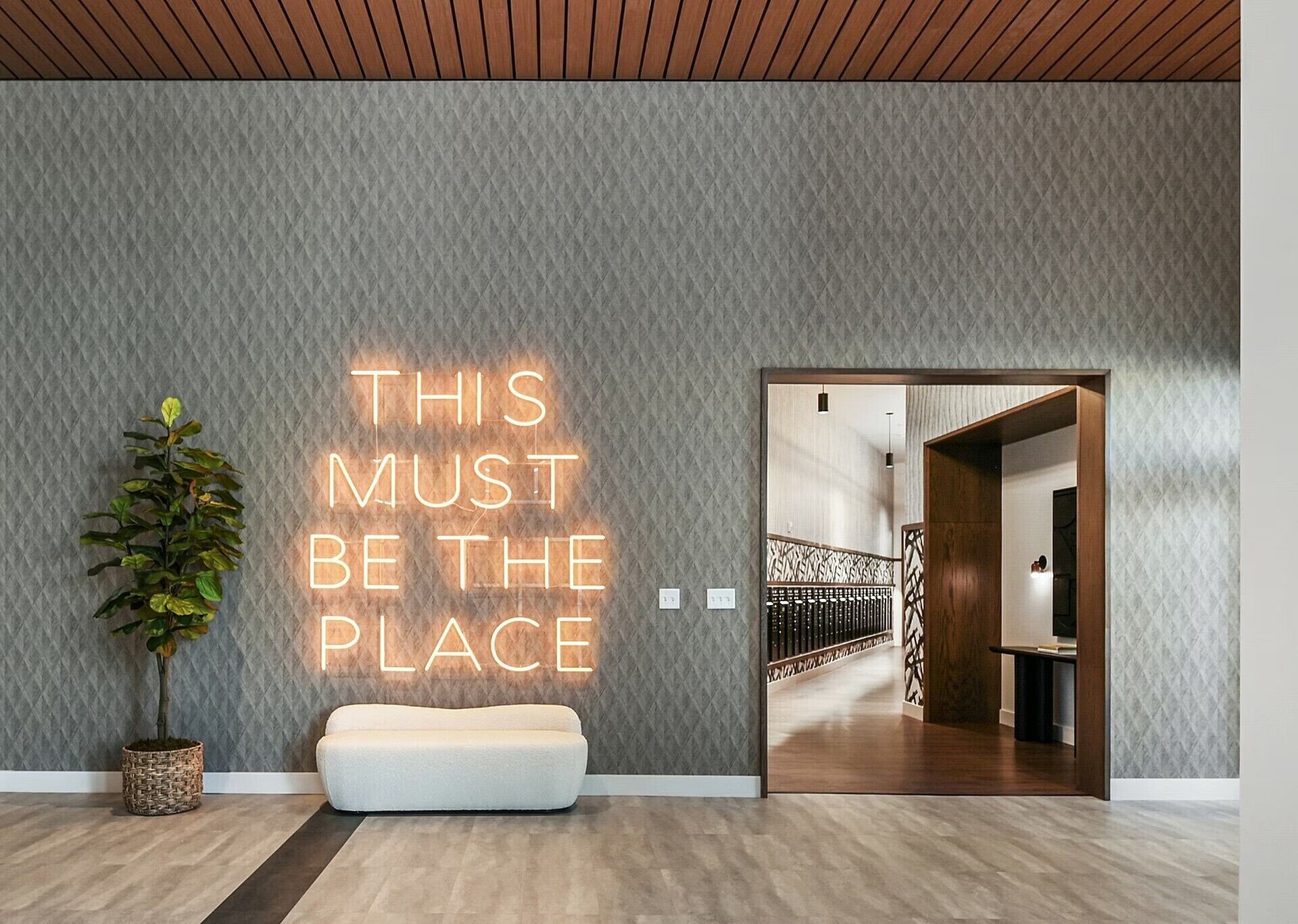 Un interior moderno con una pared con textura, un letrero de neón, una planta en maceta y un banco.