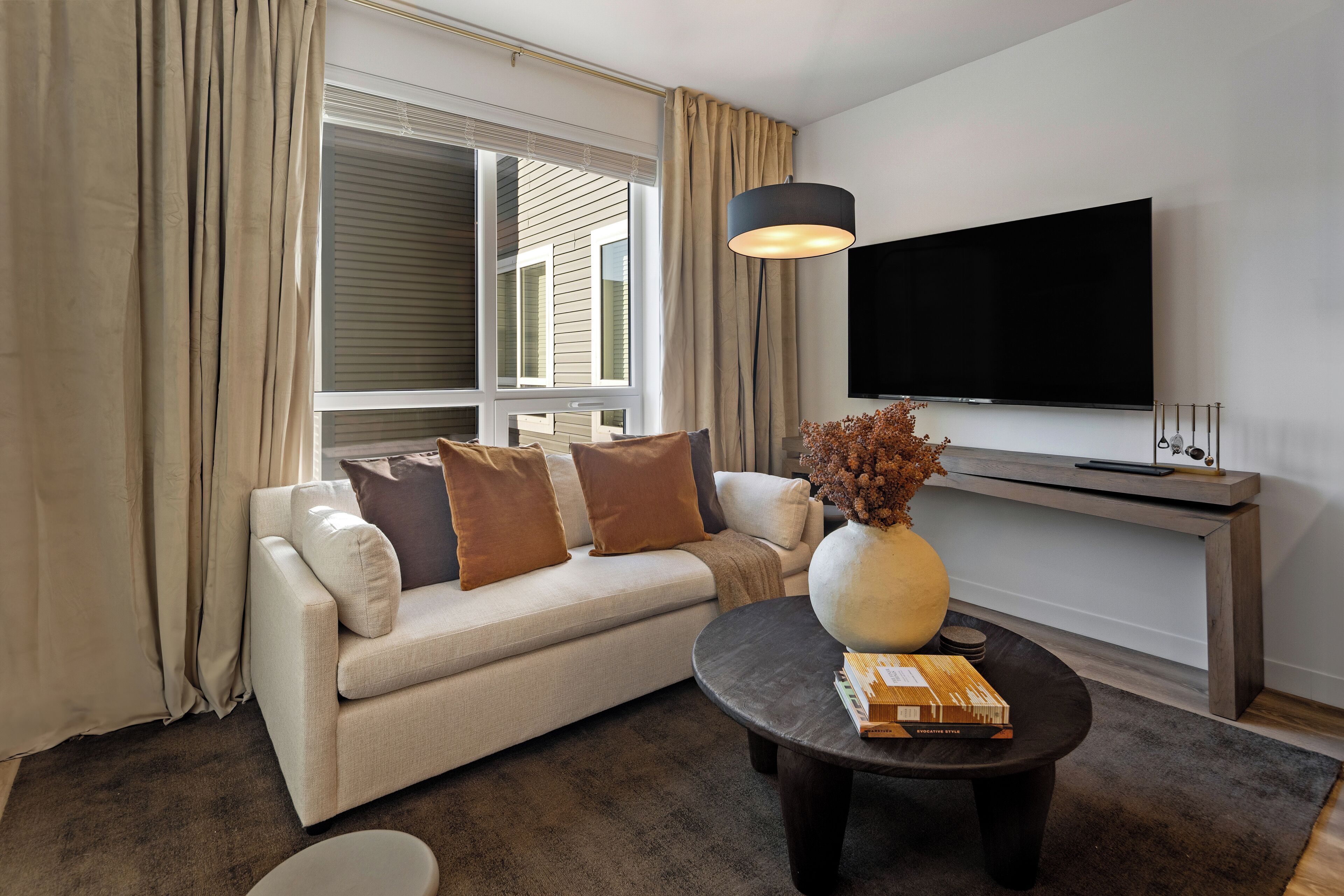 A modern living room with a sofa, a coffee table, a TV, and a window with curtains.