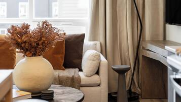 A cozy living room with a sofa, a round table, a vase with dried flowers, and a view of the city through a window.