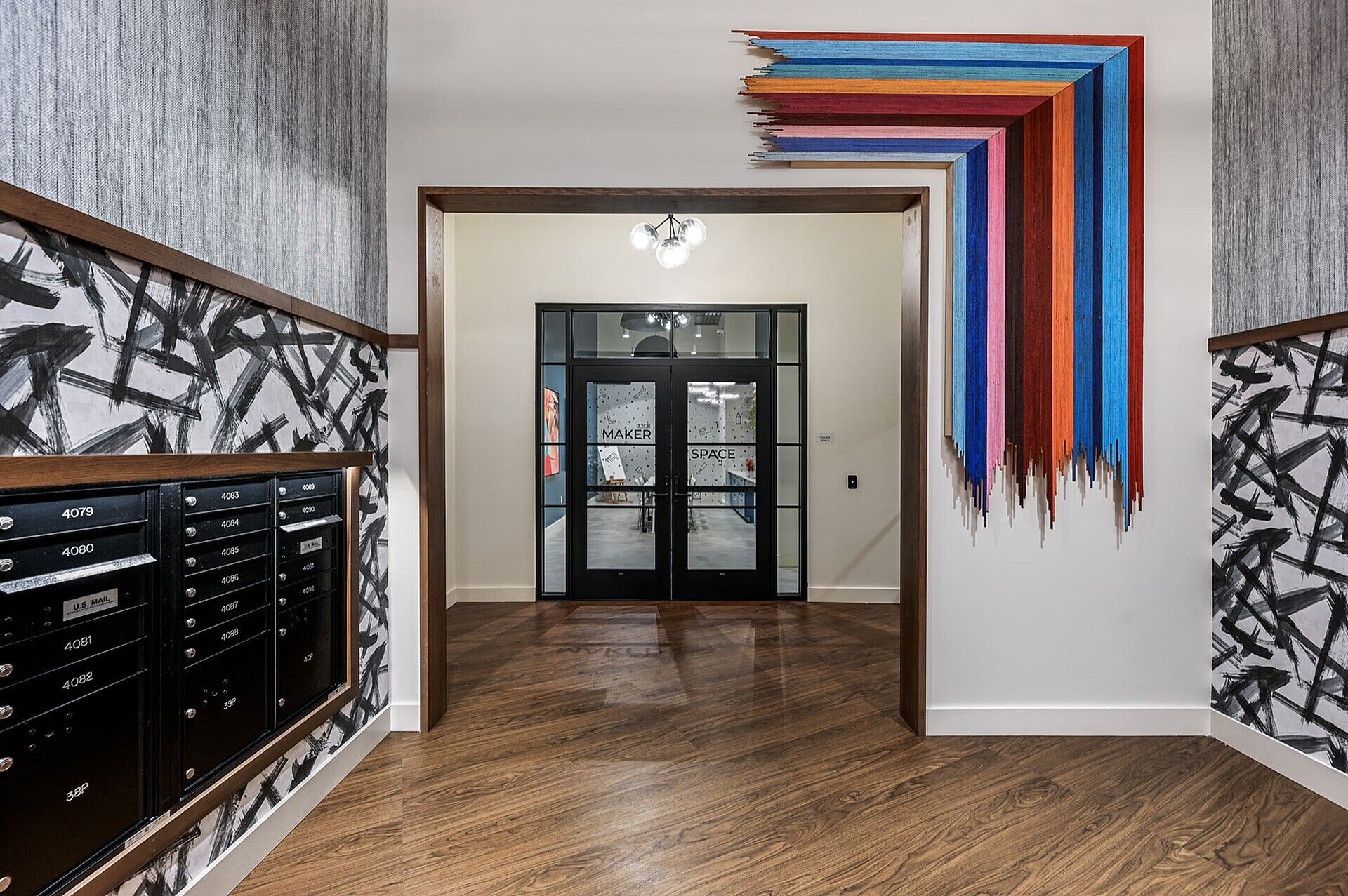 A hallway with a wooden floor, a black mailbox, and a colorful abstract art piece on the wall.