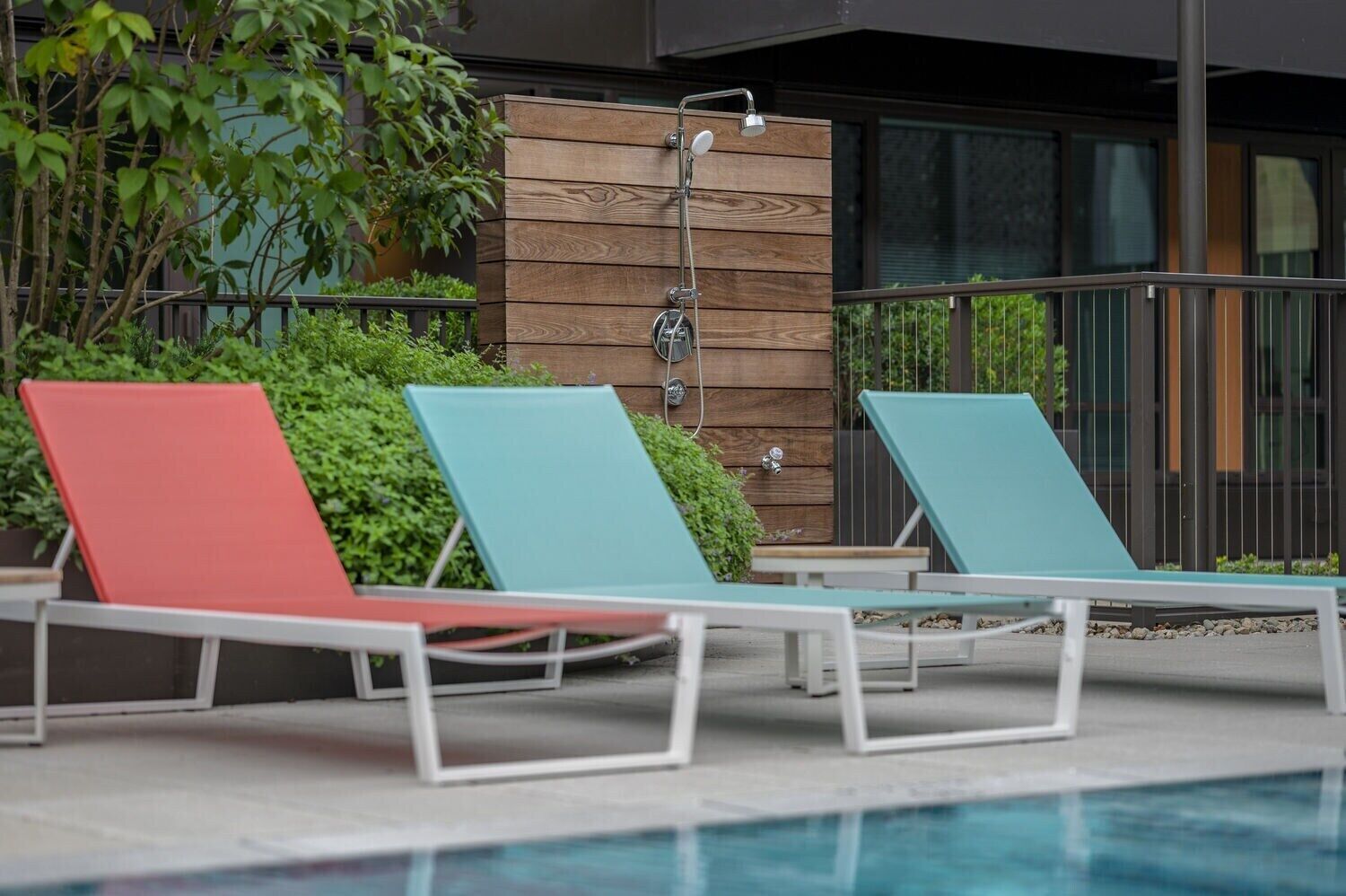 A poolside area with lounge chairs and a wooden wall with a showerhead.