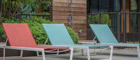 A poolside area with lounge chairs and a wooden wall with a showerhead.