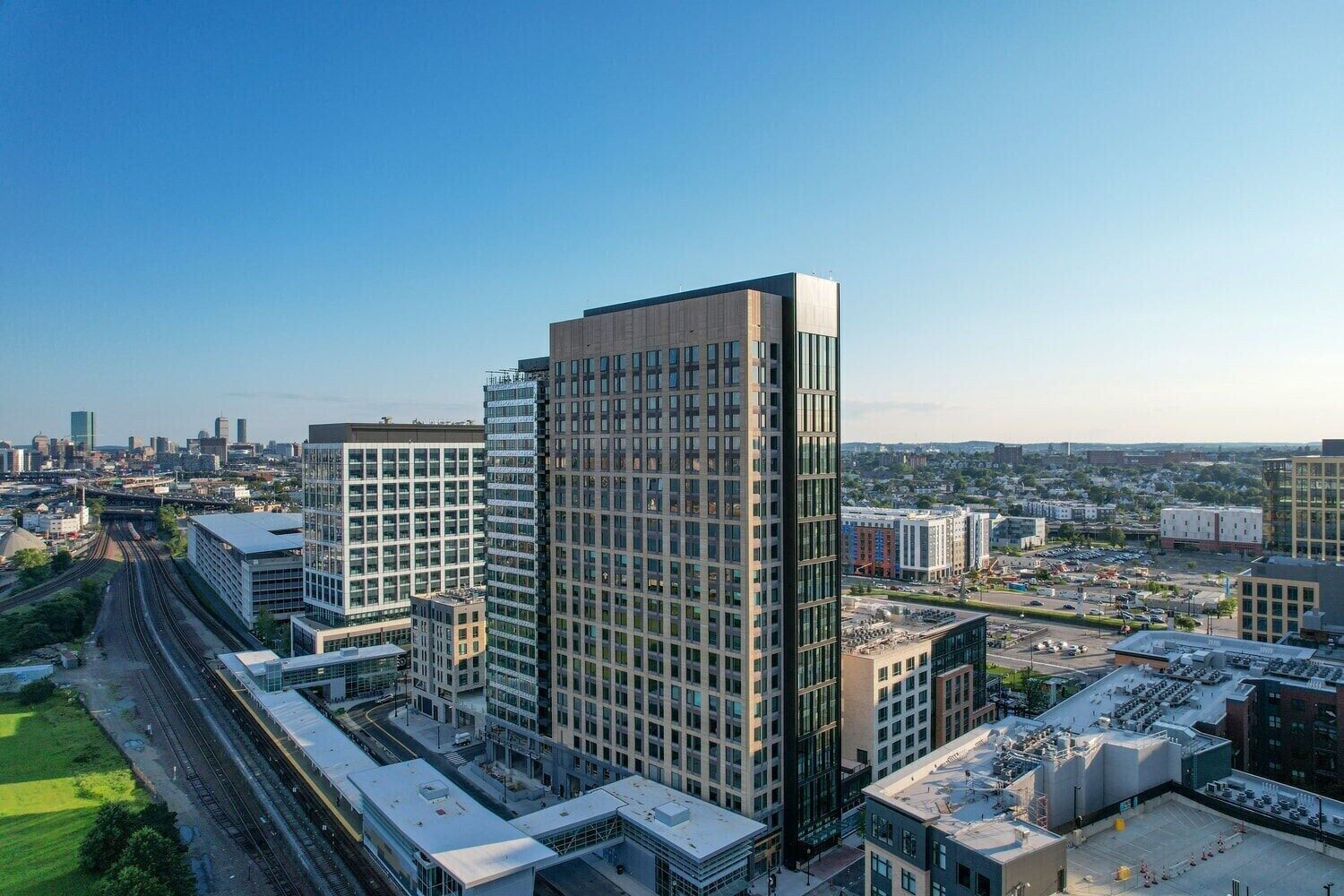 A high-rise building with a modern architectural design, surrounded by other buildings and a train track.