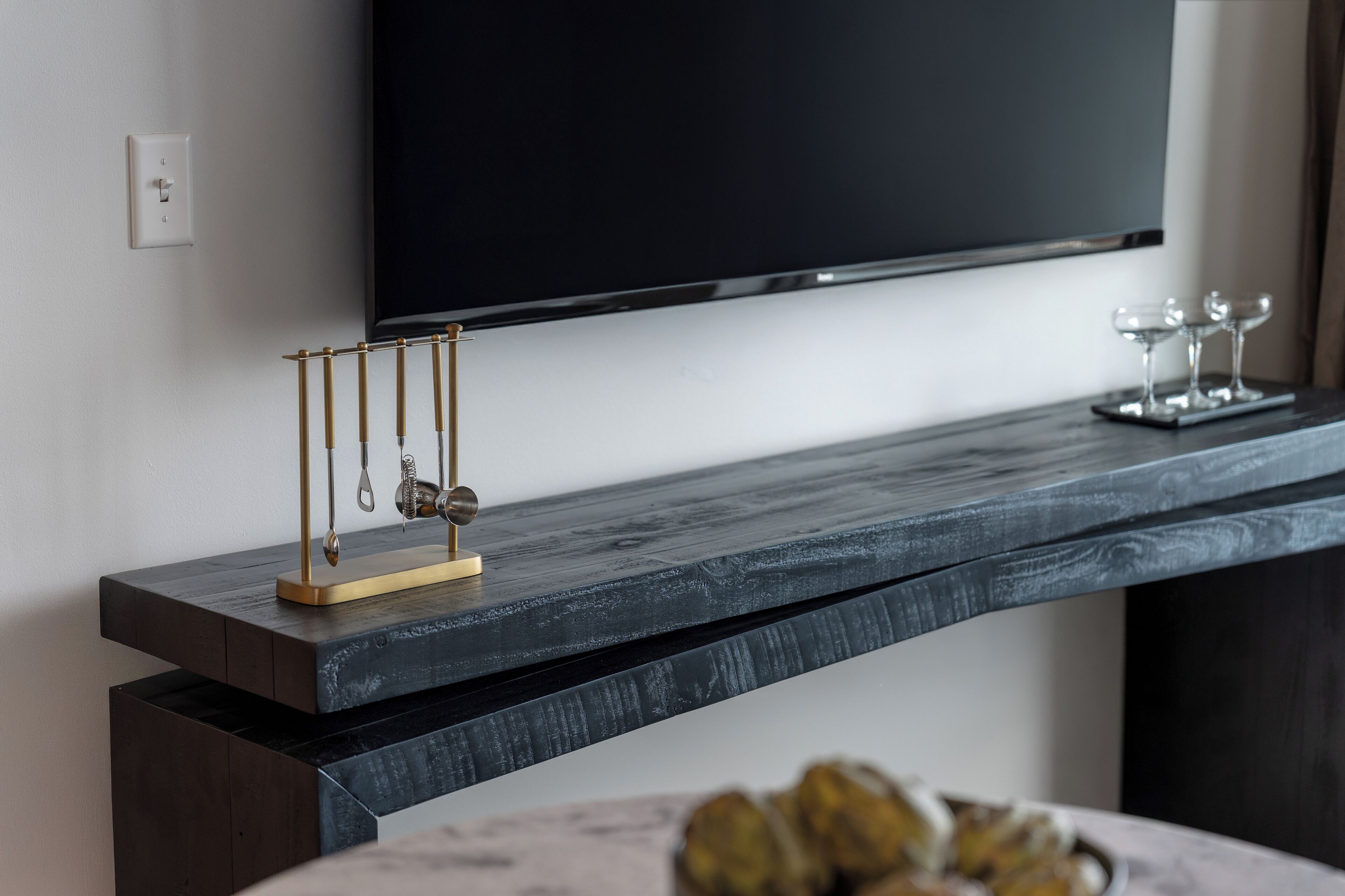A modern living room with a flat-screen TV mounted on the wall, a dark wooden console table, and a decorative metal sculpture.