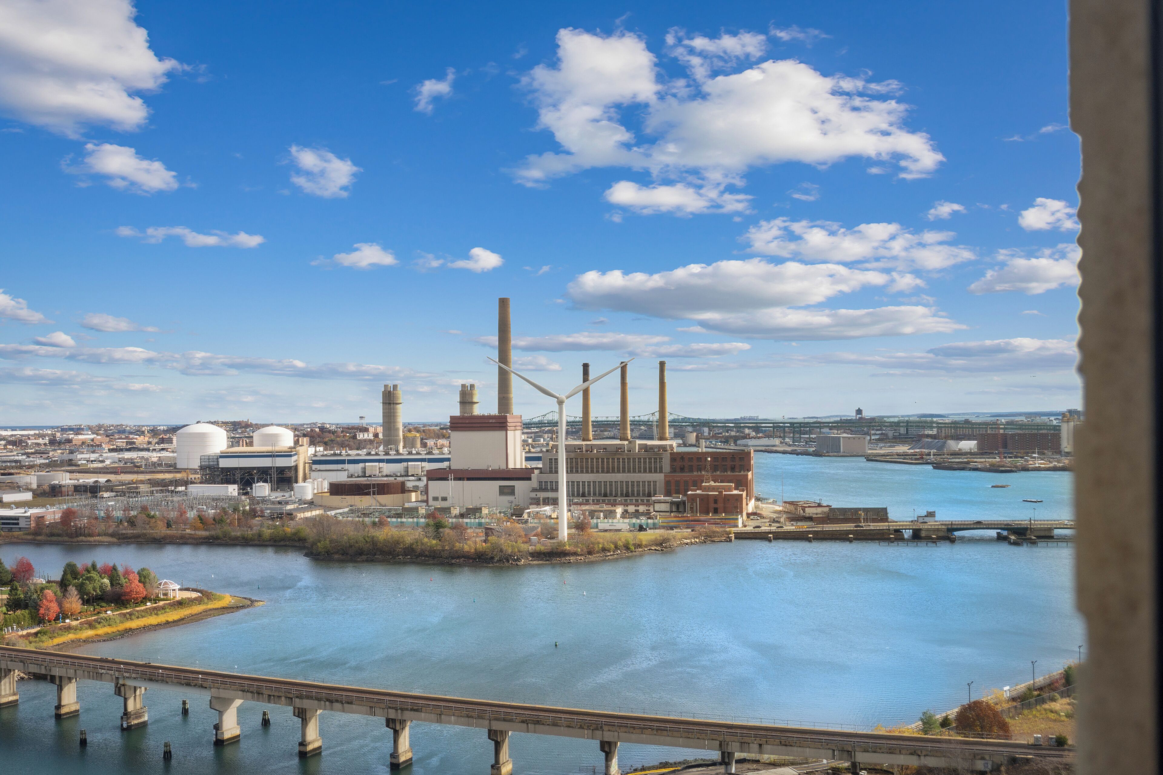 A large industrial facility with multiple smokestacks and storage tanks, located near a river with a bridge crossing.