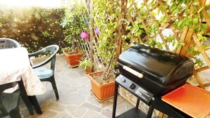 A patio with a barbecue grill, a table with a floral tablecloth, and potted plants.