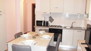 A compact kitchen with white cabinets, a microwave, a stove, and a dishwasher. There is a dining table set with plates, glasses, and cutlery.
