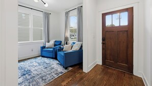 Ein Wohnzimmer mit zwei blauen Sofas, einem gemusterten Teppich, einer Holztür und einem Fenster mit Vorhängen.