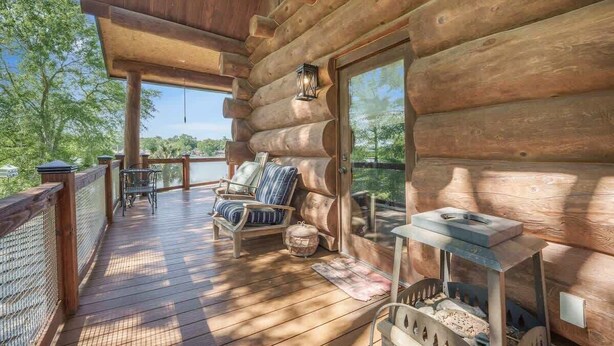 Una cabaña de madera con un balcón, una silla con cojines, un farol y una ventana con vistas a un paisaje natural.