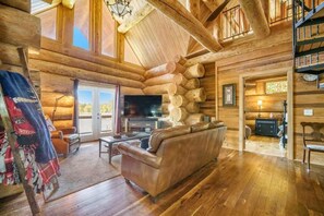 Een blokhutinterieur met een open haard, leren bank, houten vloeren en een televisie.