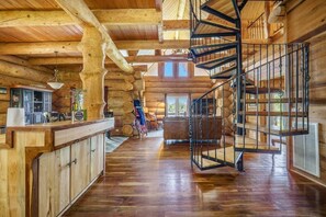 A log cabin interior with a wooden staircase, a kitchen area, and a large window. - Lakeside Log Cabin. Hot tub, Dock, Boat Lift! (Manning)
