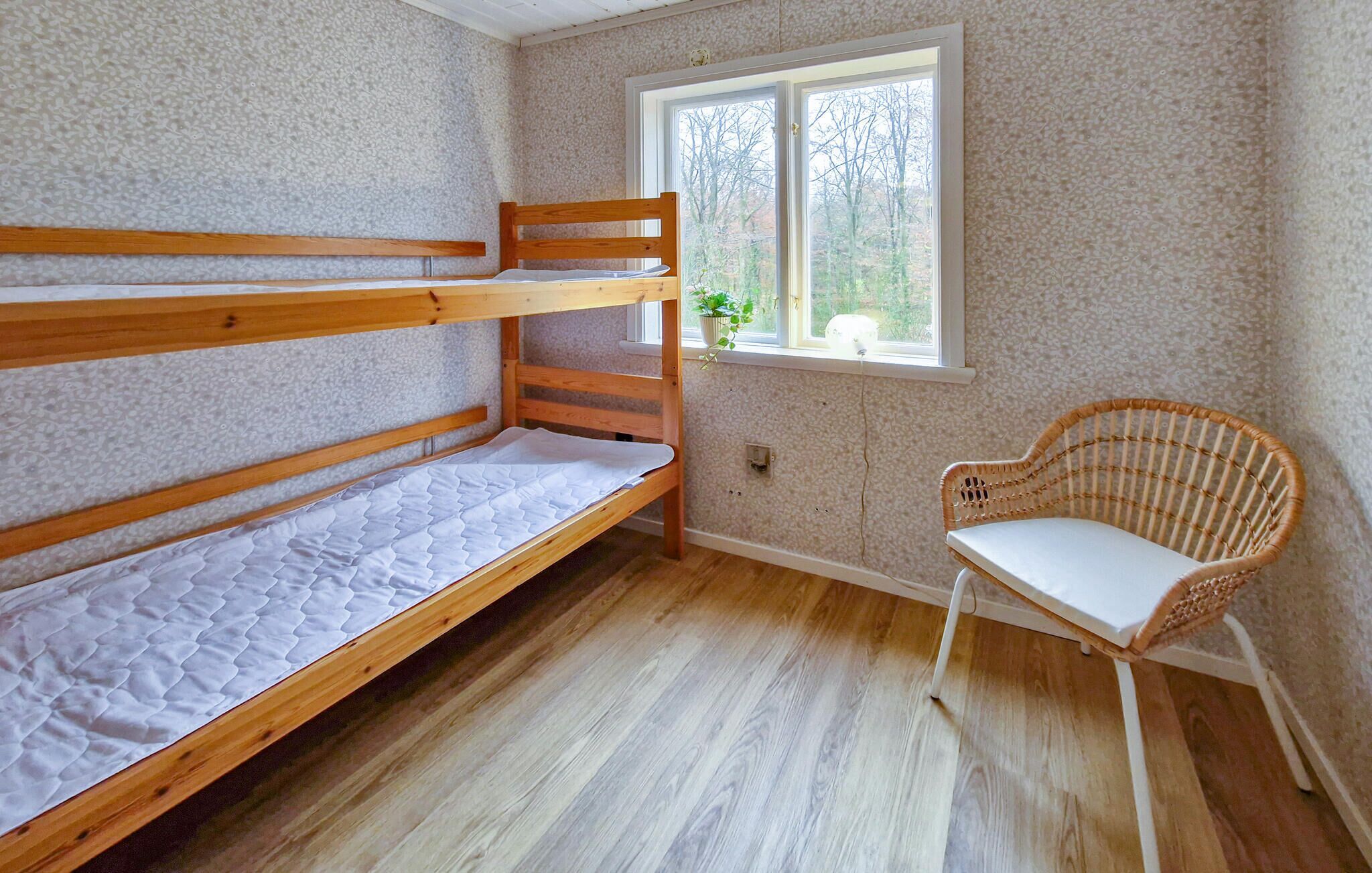 Une chambre avec un lit superposé, une chaise en osier et une fenêtre donnant sur les arbres.