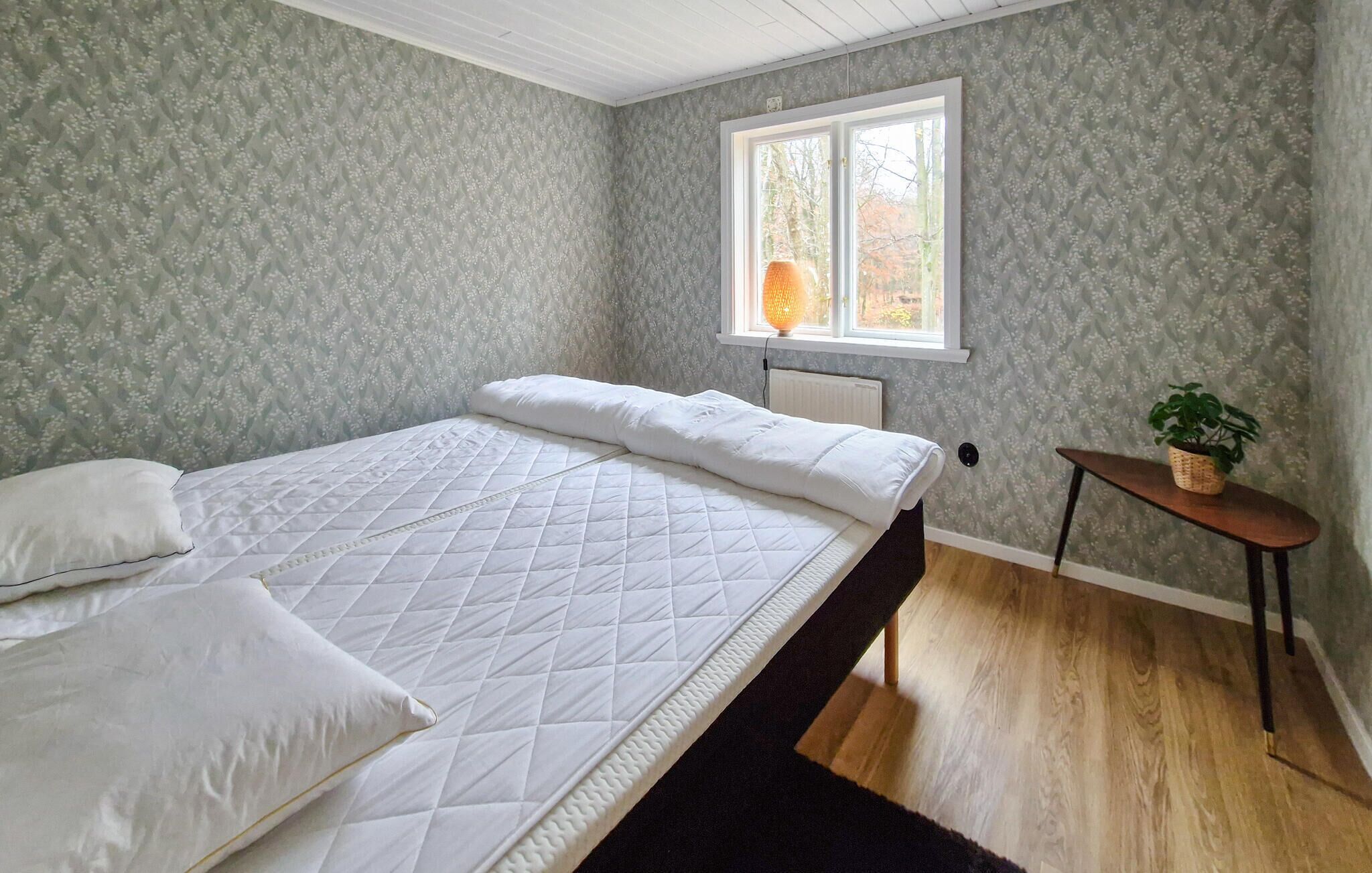 Une chambre à coucher avec un lit, une fenêtre, un radiateur et une petite table sur laquelle est posée une plante.