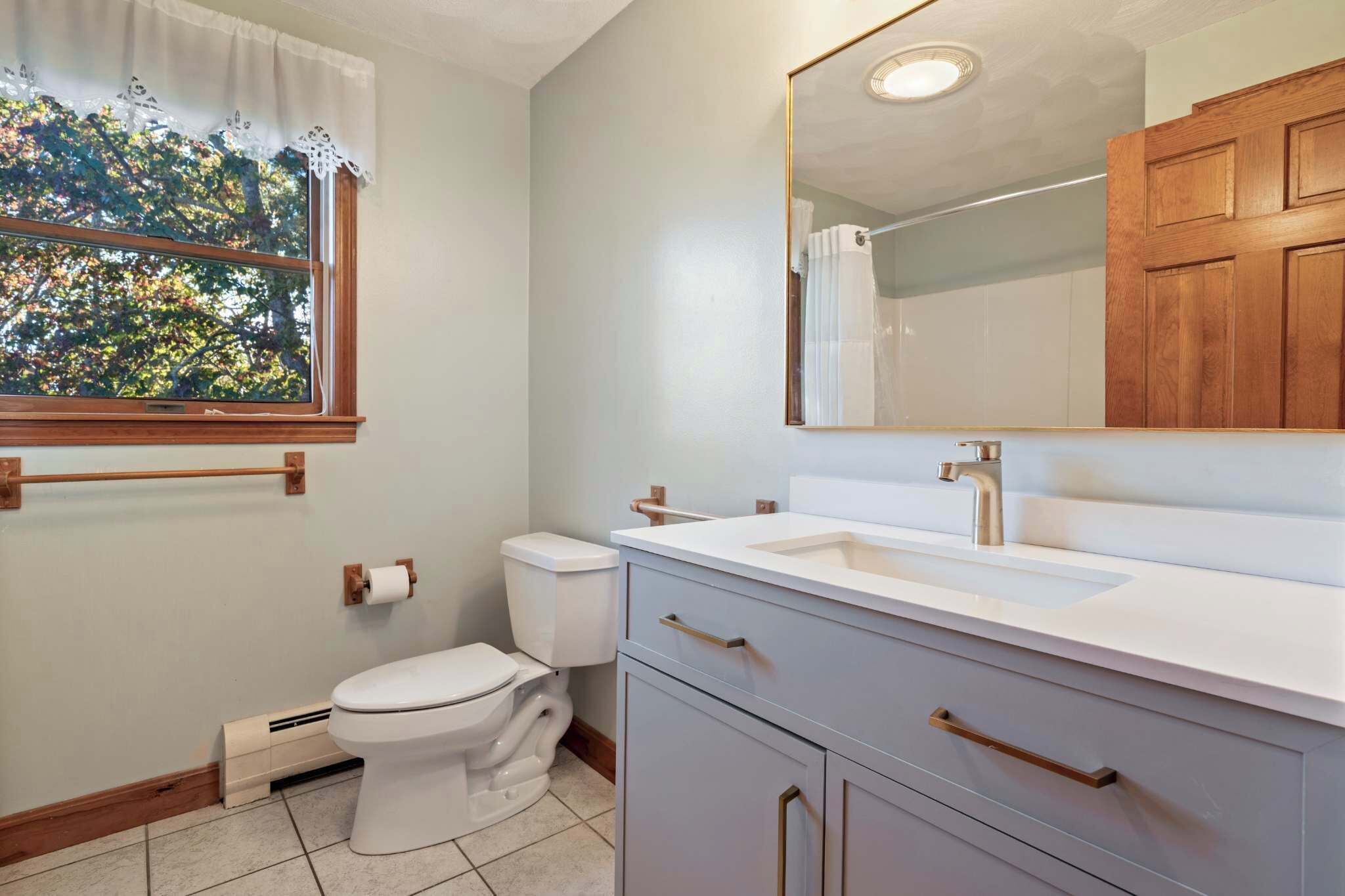 A bathroom with a toilet, sink, vanity, and a window with a view of trees.
