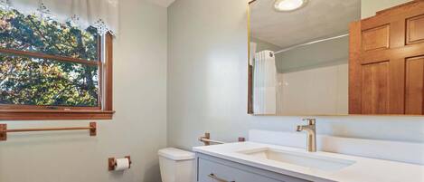 A bathroom with a toilet, sink, vanity, and a window with a view of trees.