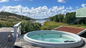 Ett bubbelbad på ett trädäck med utsikt över en sjö och en klar himmel.