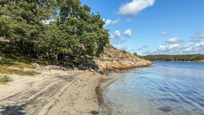 En sandstrand med klart vatten, en klippig kust och tät vegetation.