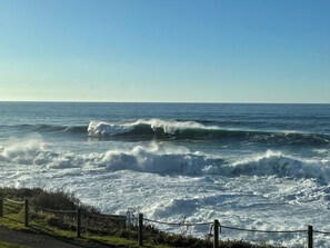 A coastal view with waves crashing onto the shore, a clear sky, and a fence along the beach. - Ocean Front-2 bedroom condo in charming Depoe Bay with rec room, pool & gym (Depoe Bay)