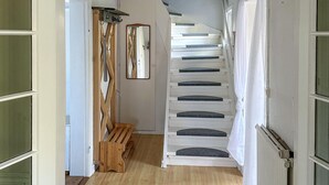 Un escalier avec des marches blanches et des contremarches sombres, menant à un palier où se trouvent un banc en bois et un porte-manteau.