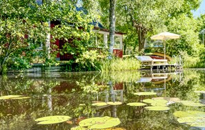 A serene outdoor area with a pond, lily pads, and a small table with an umbrella. - Gorgeous Lake House in Ålberga (Ålberga)
