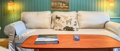 A room with a teal wall, a white sofa with patterned cushions, a wooden coffee table with a magazine, and two wall-mounted lamps.
