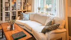 Un salon avec un canapé blanc, une table basse en bois, une bibliothèque et une fenêtre avec des rideaux.