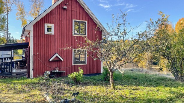 Ein rotes Bauernhaus mit Satteldach, einer kleinen Veranda und einem Garten mit Baum und Rasen.