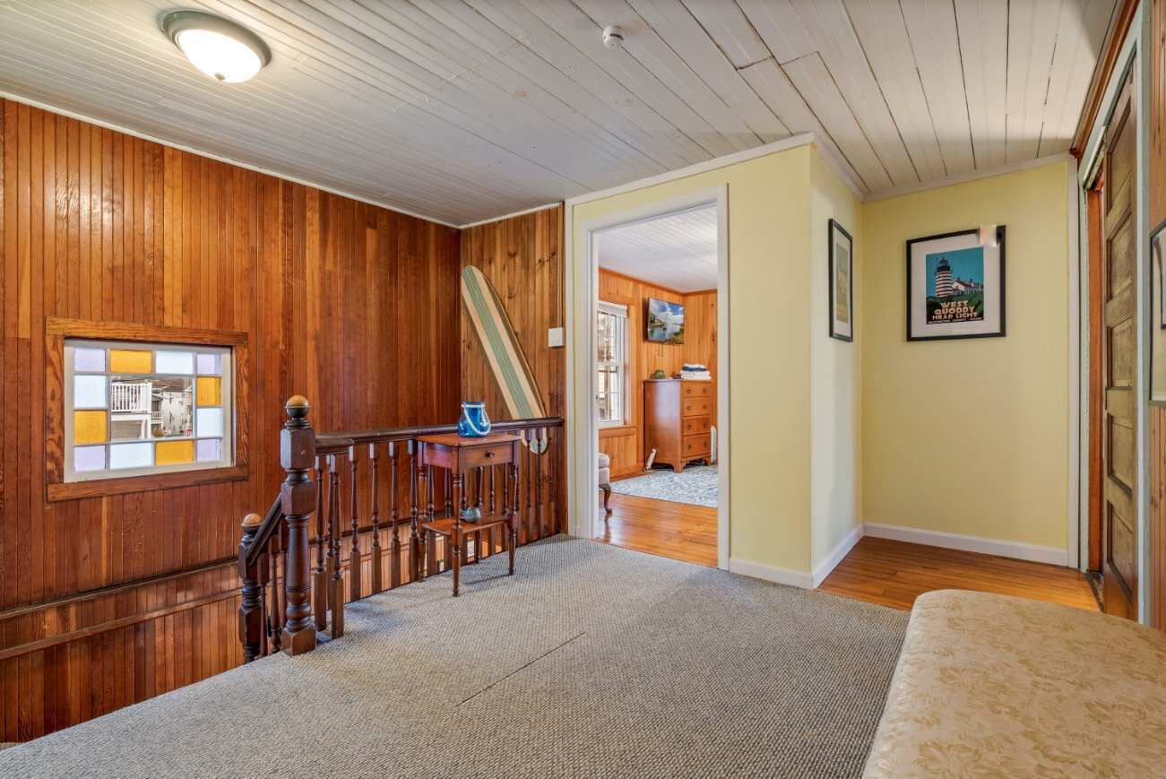 A spacious room with a wooden staircase, a small table with a blue object, and a framed picture on the wall.
