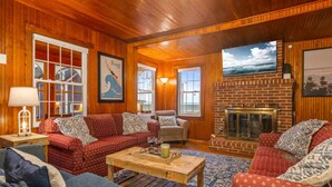 A cozy living room with wooden walls and floors, featuring a fireplace, a television, and comfortable seating. - Danemead Cottage - For 10ppl (Old Orchard Beach)