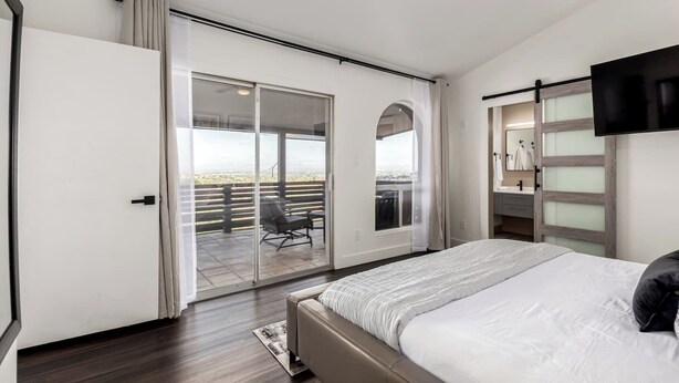 Una camera da letto con un grande letto, una porta scorrevole in vetro che dà su un balcone e una TV montata a parete.