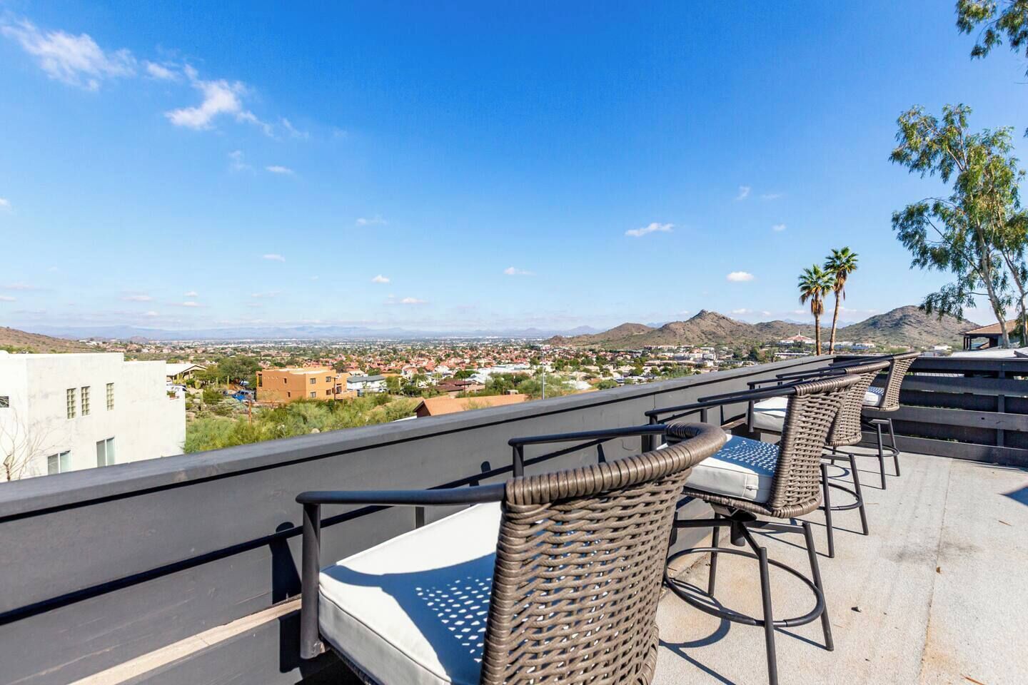 A rooftop terrace with wicker chairs and a view of a cityscape and mountains.