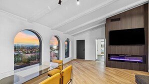 Un ampio soggiorno con una grande televisione, pavimento in legno e vista sulla città attraverso finestre ad arco.