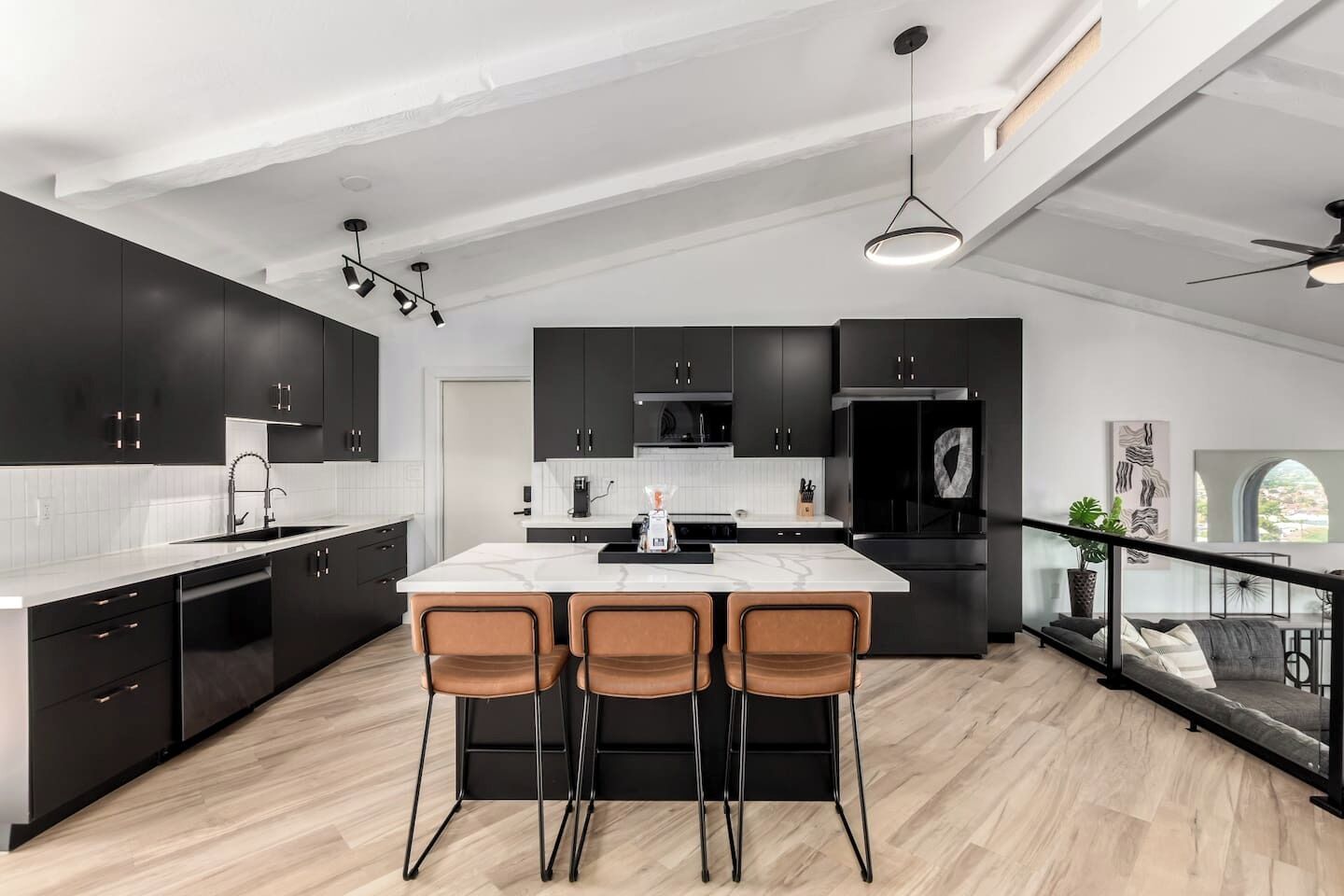 Une cuisine moderne avec des meubles de couleur sombre, un îlot en marbre et trois tabourets de bar.