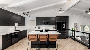 Una cucina moderna con mobili scuri, un'isola in marmo e tre sgabelli da bar.