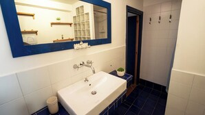 Un baño con un lavamanos blanco, suelo de azulejos azules, un espejo con marco azul y una zona de ducha.