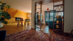 Un amplio salón con un gran tapete, sillas amarillas, una mesa de comedor y una estantería.