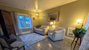 Ein Wohnzimmer mit Holzboden, zwei Sofas, einem Sessel, einem Teppich, einer Lampe, einem Spiegel und einer Topfpflanze.