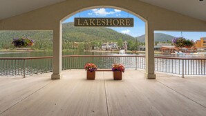 Blick auf einen See mit einem Schild mit der Aufschrift "LAKESHORE", Bänken mit Blumenarrangements und im Hintergrund eine Seeblick und Gebäude.