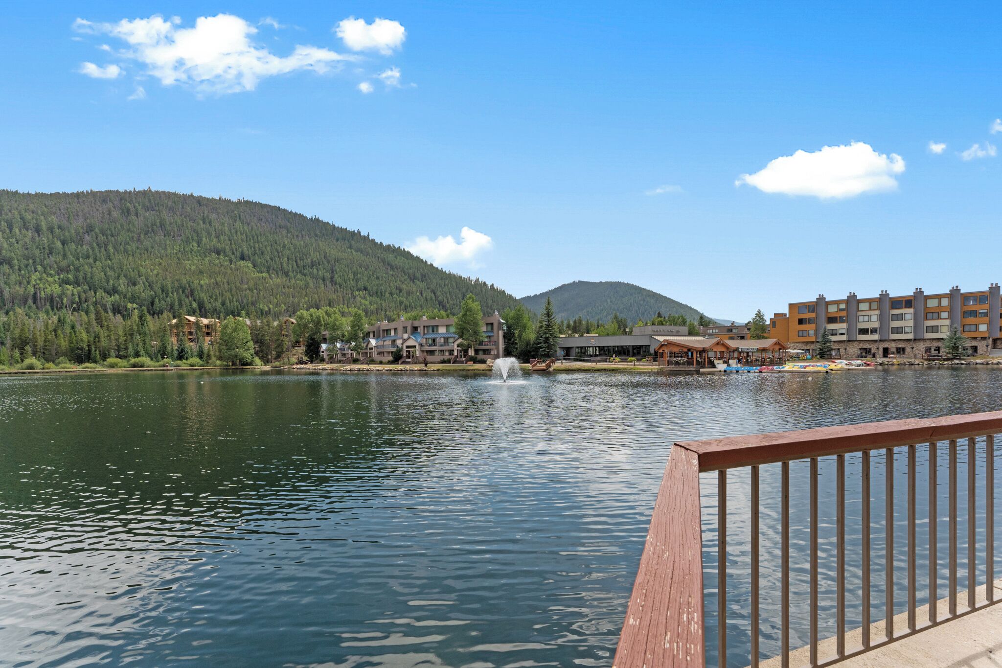Järvi, jossa on suihkulähde, ja sen ympärillä on rakennuksia sekä metsäinen kukkula.