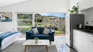 A modern living room with a sofa, a coffee table, and a view of a garden through large windows.